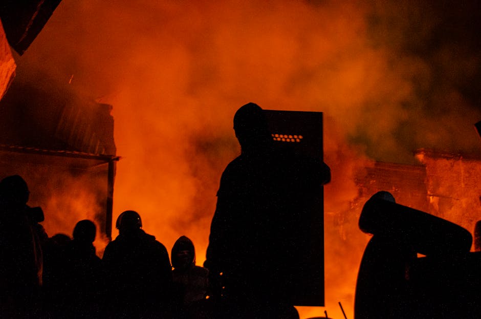 Silhouettes of protesters and smoke against fiery night backdrop in Lviv.